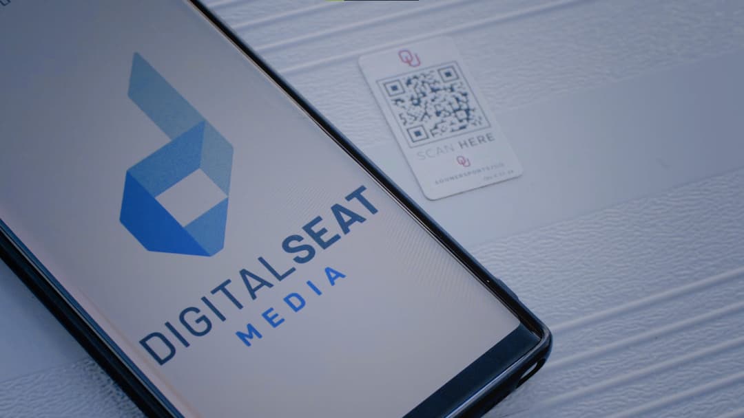 Smartphone lying beside a DigitalSeat QR code tag mounted on a stadium seat