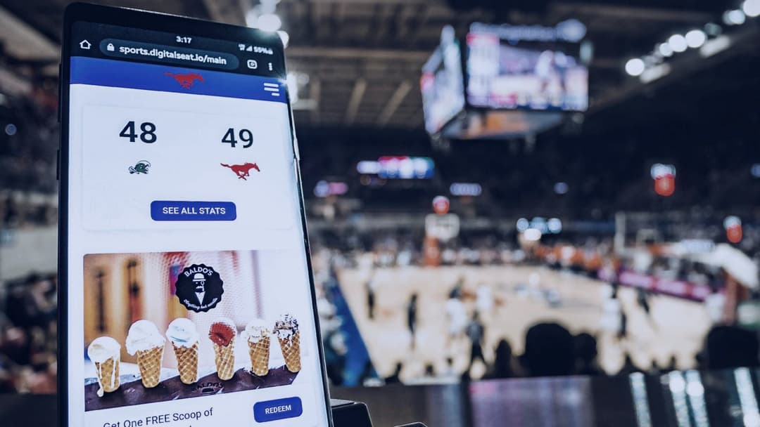 Fan holding up a phone with live game stats inside a packed basketball arena